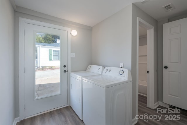 clothes washing area with laundry area, wood finished floors, washing machine and dryer, and visible vents