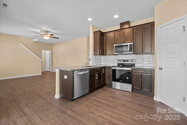 kitchen with dark brown cabinetry, stainless steel appliances, a peninsula, a sink, and backsplash