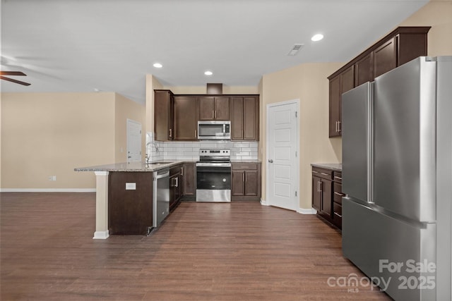 kitchen with dark brown cabinetry, backsplash, light stone countertops, stainless steel appliances, and a sink