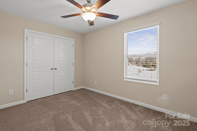 unfurnished bedroom featuring carpet floors, a closet, baseboards, and a ceiling fan