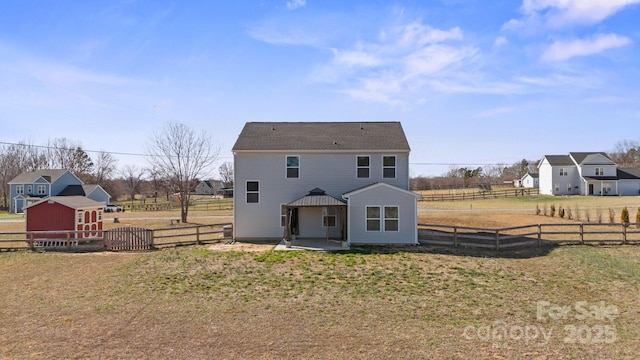 back of property with a rural view, fence, a lawn, and a patio