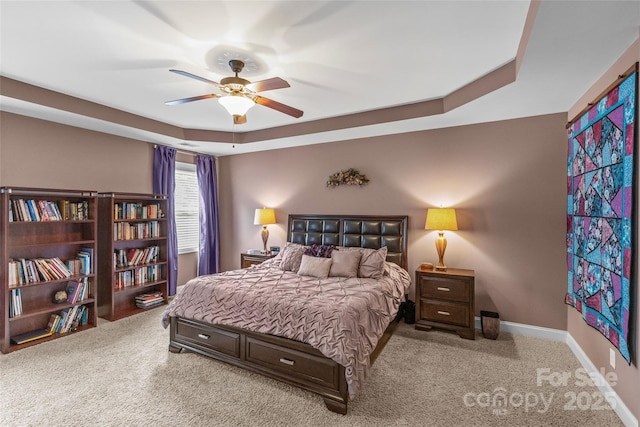 bedroom with carpet floors, a tray ceiling, baseboards, and a ceiling fan