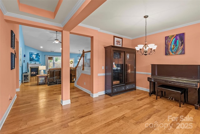 living area featuring baseboards, a glass covered fireplace, light wood-style flooring, stairway, and ornamental molding