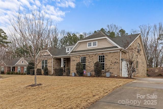 view of front of house with a front yard, brick siding, driveway, and roof with shingles