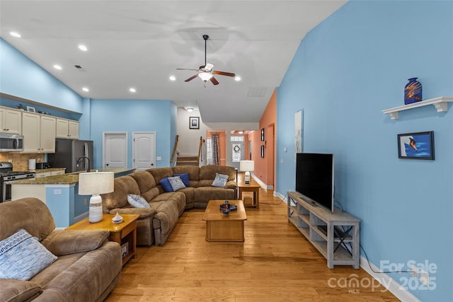 living room featuring light wood-style floors, visible vents, stairs, and high vaulted ceiling