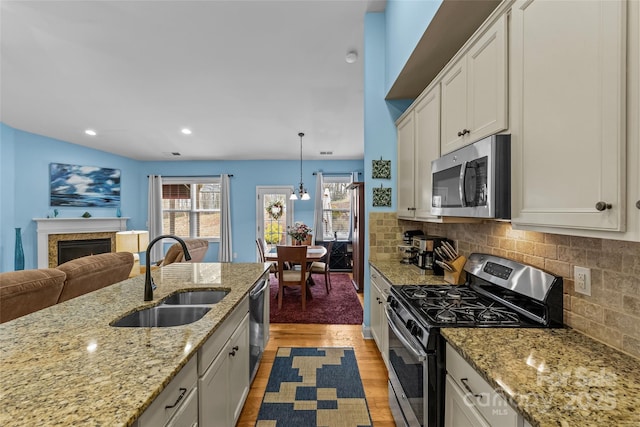 kitchen featuring light wood finished floors, backsplash, stainless steel appliances, a fireplace, and a sink