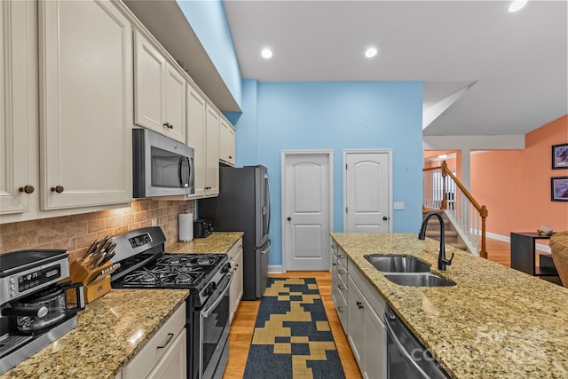 kitchen with light stone counters, stainless steel appliances, backsplash, white cabinetry, and a sink