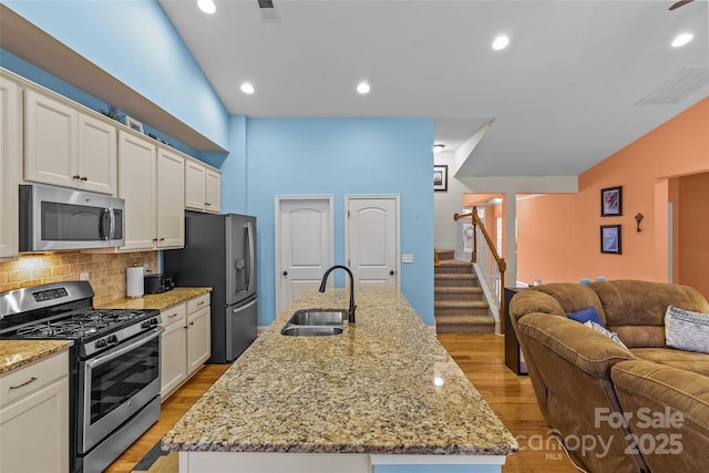 kitchen featuring a center island with sink, light wood-style flooring, appliances with stainless steel finishes, open floor plan, and a sink