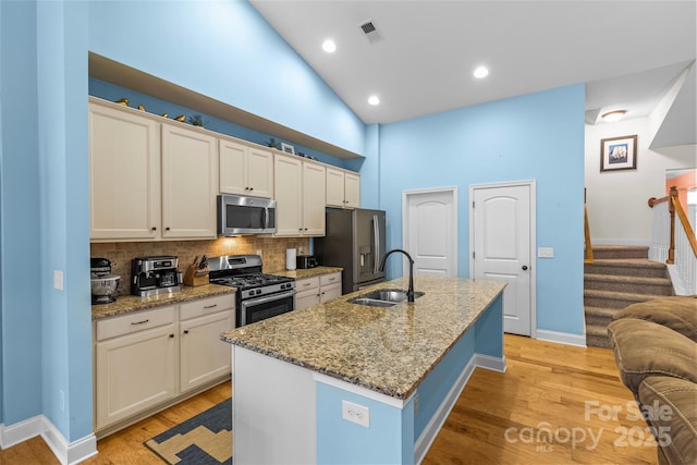 kitchen with a center island with sink, visible vents, light wood-style flooring, stainless steel appliances, and a sink