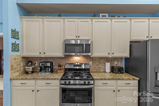 kitchen with appliances with stainless steel finishes, white cabinetry, light stone counters, and decorative backsplash