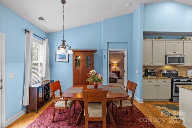 dining room featuring vaulted ceiling, light wood-type flooring, visible vents, and baseboards