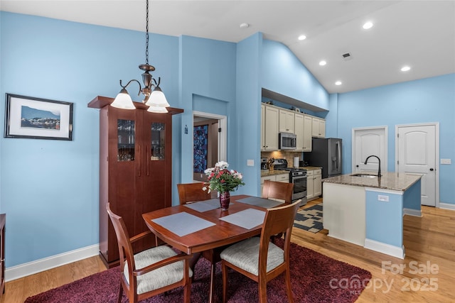 dining room with a chandelier, light wood-type flooring, high vaulted ceiling, and baseboards