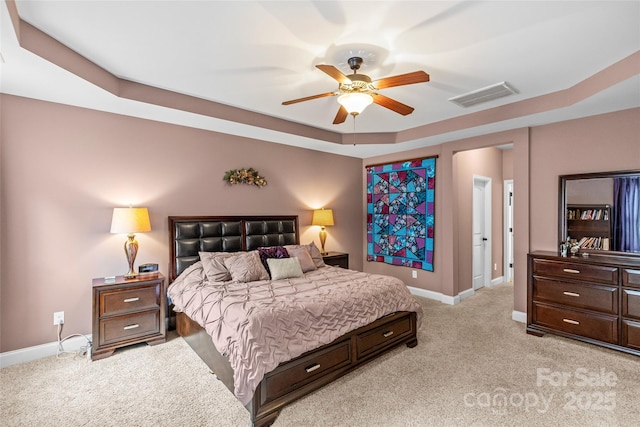 bedroom featuring light colored carpet, baseboards, visible vents, and a tray ceiling