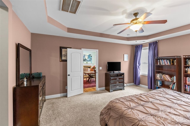 bedroom with a tray ceiling, light colored carpet, visible vents, and baseboards