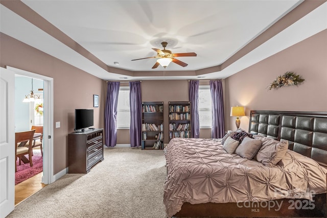 bedroom with light colored carpet, a tray ceiling, multiple windows, and baseboards