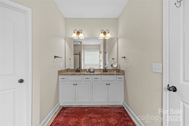 full bathroom featuring a sink, a shower stall, baseboards, and double vanity