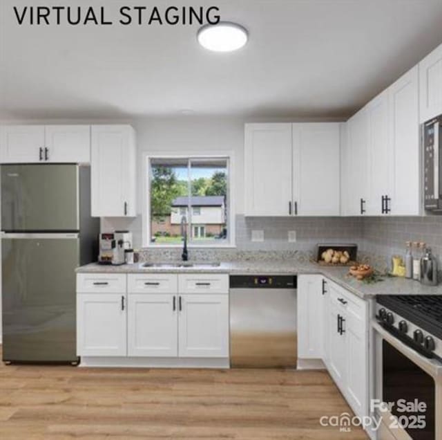 kitchen with backsplash, light wood-style flooring, appliances with stainless steel finishes, white cabinetry, and a sink