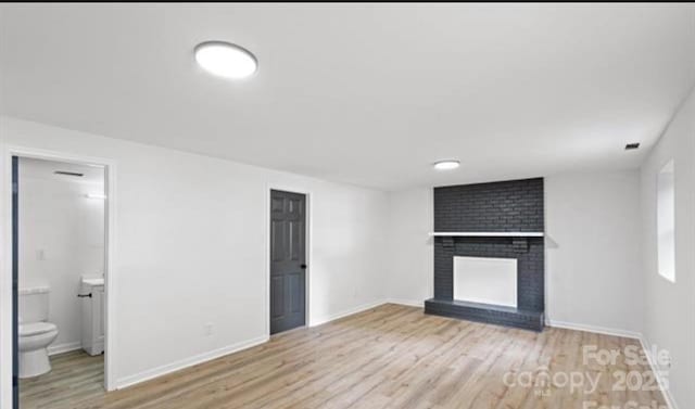 unfurnished living room featuring baseboards, a brick fireplace, and light wood-style floors