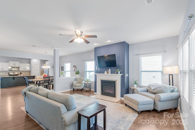 living area featuring a fireplace with flush hearth, ceiling fan with notable chandelier, wood finished floors, and baseboards