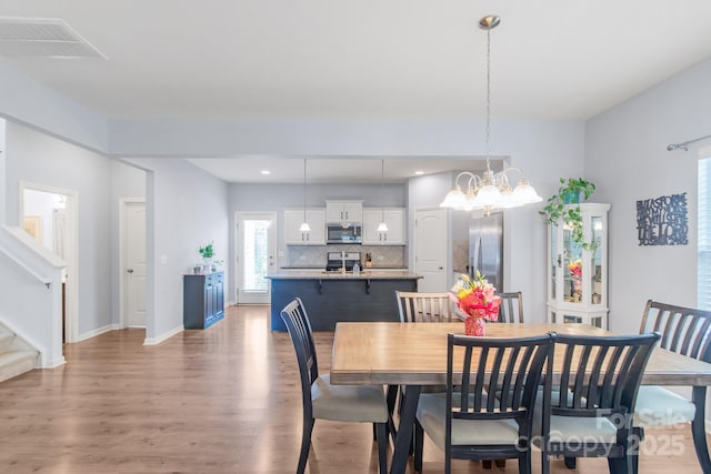 dining space with light wood-style flooring, visible vents, baseboards, stairs, and an inviting chandelier