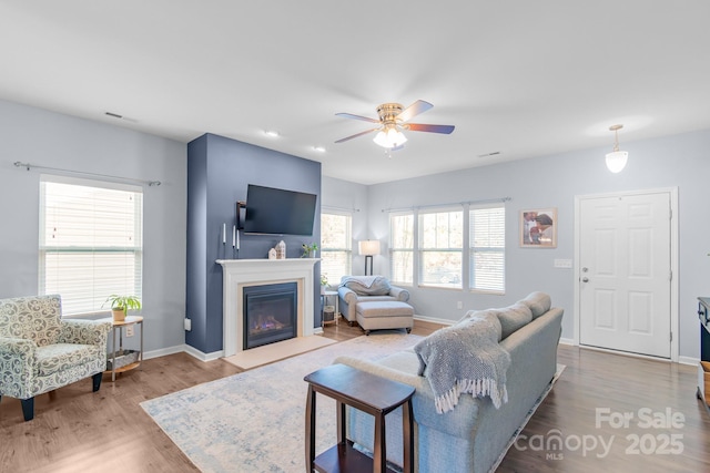 living room with baseboards, a fireplace with flush hearth, visible vents, and wood finished floors