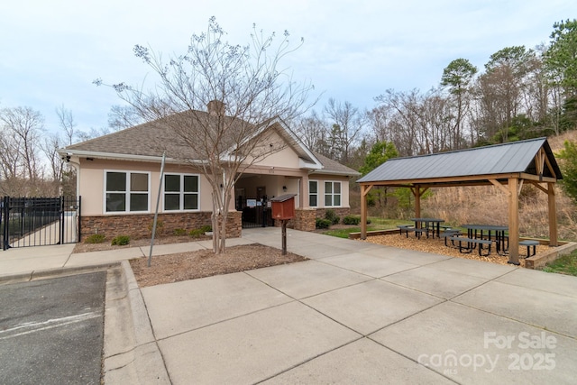 view of front of home featuring stone siding, concrete driveway, a gazebo, stucco siding, and a chimney