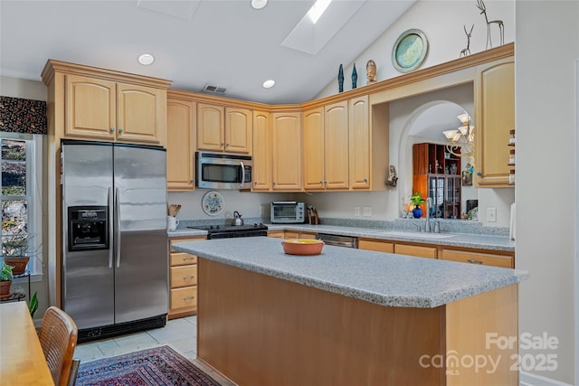 kitchen with a center island, stainless steel appliances, light brown cabinetry, lofted ceiling with skylight, and a sink