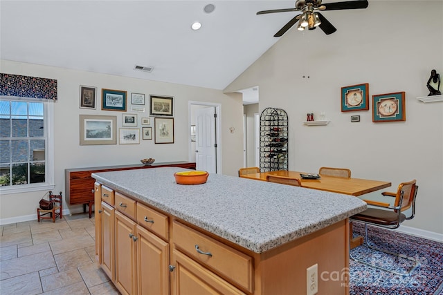 kitchen featuring stone tile floors, baseboards, visible vents, a ceiling fan, and a center island