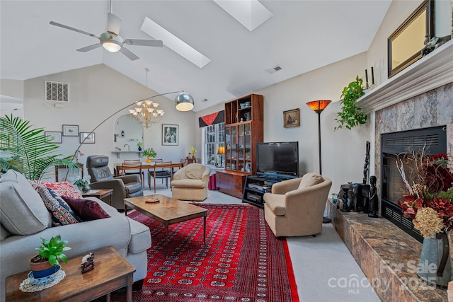 living room with ceiling fan with notable chandelier, a premium fireplace, visible vents, lofted ceiling with skylight, and carpet