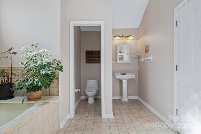 full bath featuring toilet, a garden tub, baseboards, and tile patterned floors