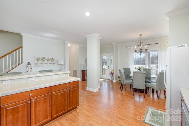 kitchen with light wood finished floors, ornamental molding, brown cabinets, freestanding refrigerator, and pendant lighting