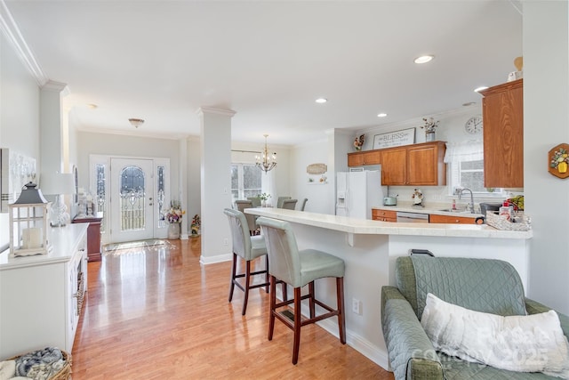 kitchen with a breakfast bar, light countertops, brown cabinetry, white fridge with ice dispenser, and a peninsula