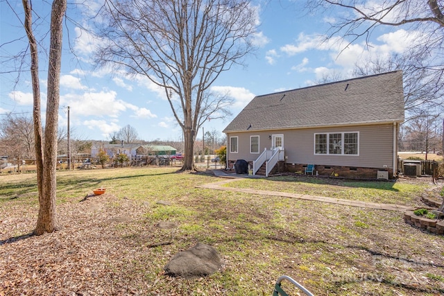 rear view of property with a shingled roof, crawl space, a yard, and central air condition unit