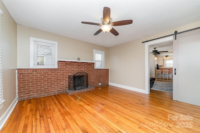 unfurnished living room featuring a brick fireplace, a barn door, a textured ceiling, and light wood-style floors