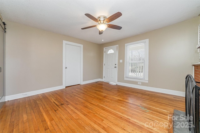 foyer featuring baseboards, ceiling fan, a brick fireplace, and light wood-style floors