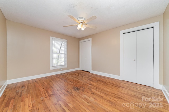 unfurnished bedroom with a textured ceiling, light wood finished floors, two closets, and baseboards