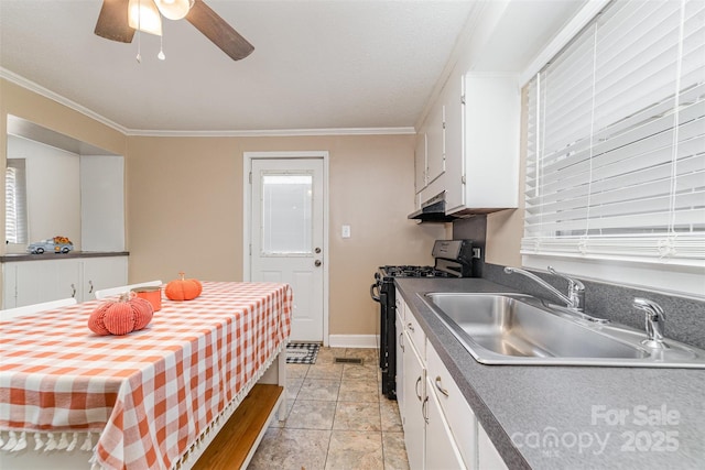 kitchen featuring dark countertops, black range with gas stovetop, crown molding, white cabinetry, and a sink