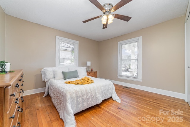 bedroom with ceiling fan, wood finished floors, visible vents, and baseboards