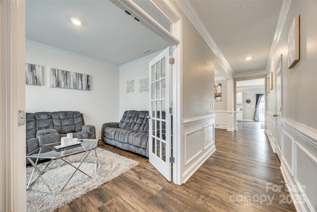 living area featuring visible vents, ornamental molding, a decorative wall, and dark wood-style flooring