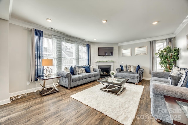 living area with a fireplace, wood finished floors, visible vents, baseboards, and ornamental molding