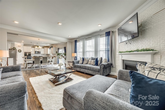 living room featuring a fireplace, crown molding, visible vents, brick wall, and wood finished floors