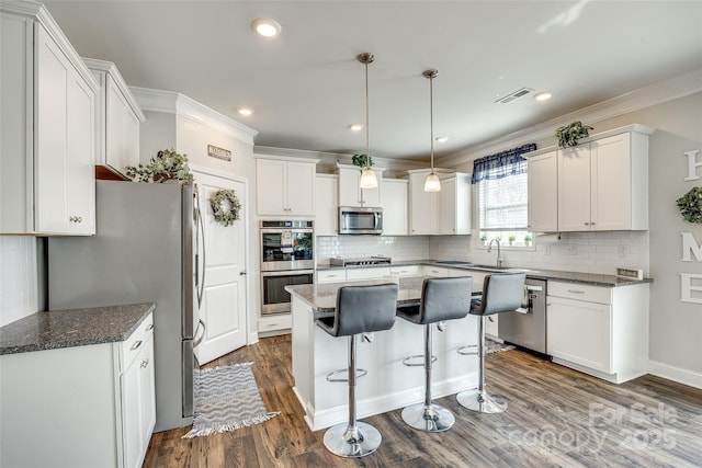 kitchen with a kitchen island, white cabinetry, stainless steel appliances, and dark stone countertops