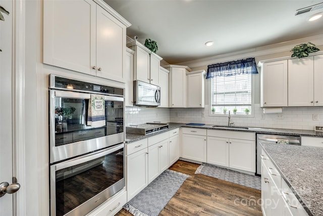 kitchen featuring decorative backsplash, appliances with stainless steel finishes, dark stone countertops, white cabinetry, and a sink