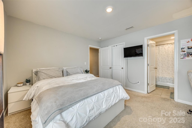 bedroom with a closet, visible vents, light carpet, ensuite bath, and baseboards