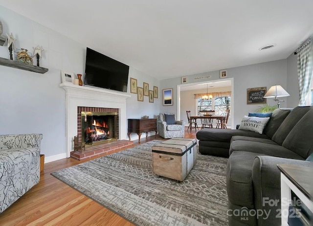 living area with baseboards, visible vents, wood finished floors, an inviting chandelier, and a fireplace