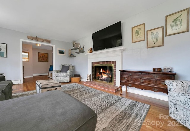 living area featuring a baseboard radiator, a fireplace, baseboards, and wood finished floors