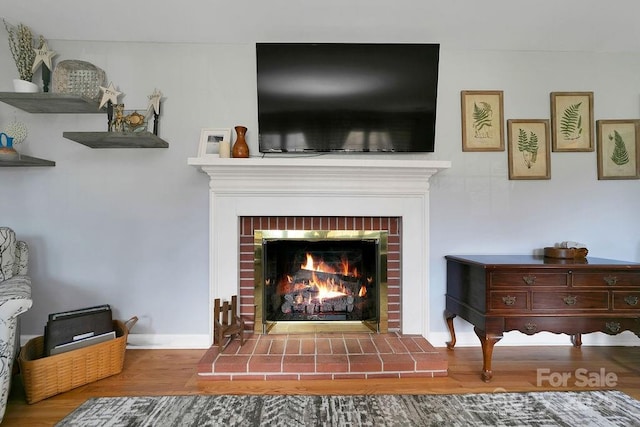 living room featuring a brick fireplace, wood finished floors, and baseboards