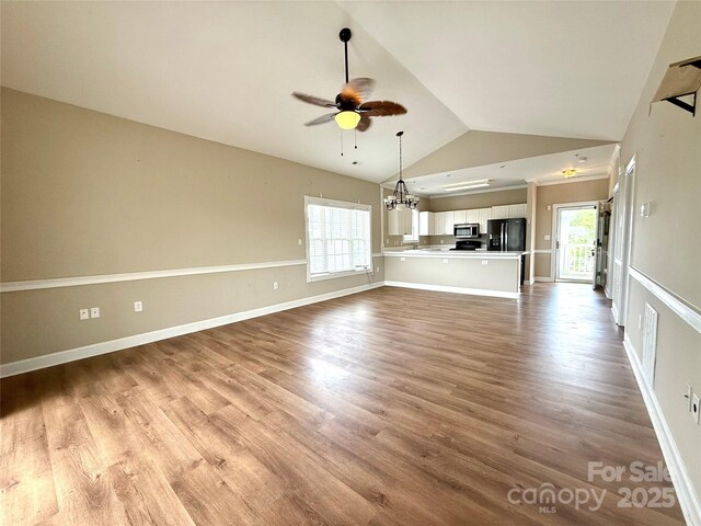 unfurnished living room with ceiling fan with notable chandelier, baseboards, wood finished floors, and lofted ceiling