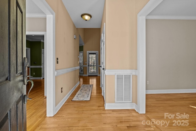 corridor with light wood-style floors, visible vents, crown molding, and baseboards