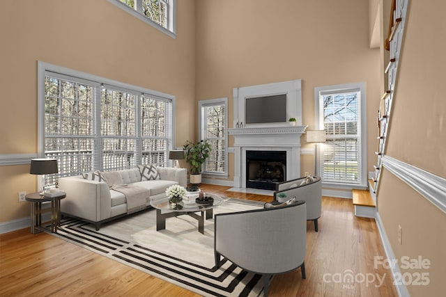 living room with light wood-style floors, baseboards, a high ceiling, and a fireplace with flush hearth